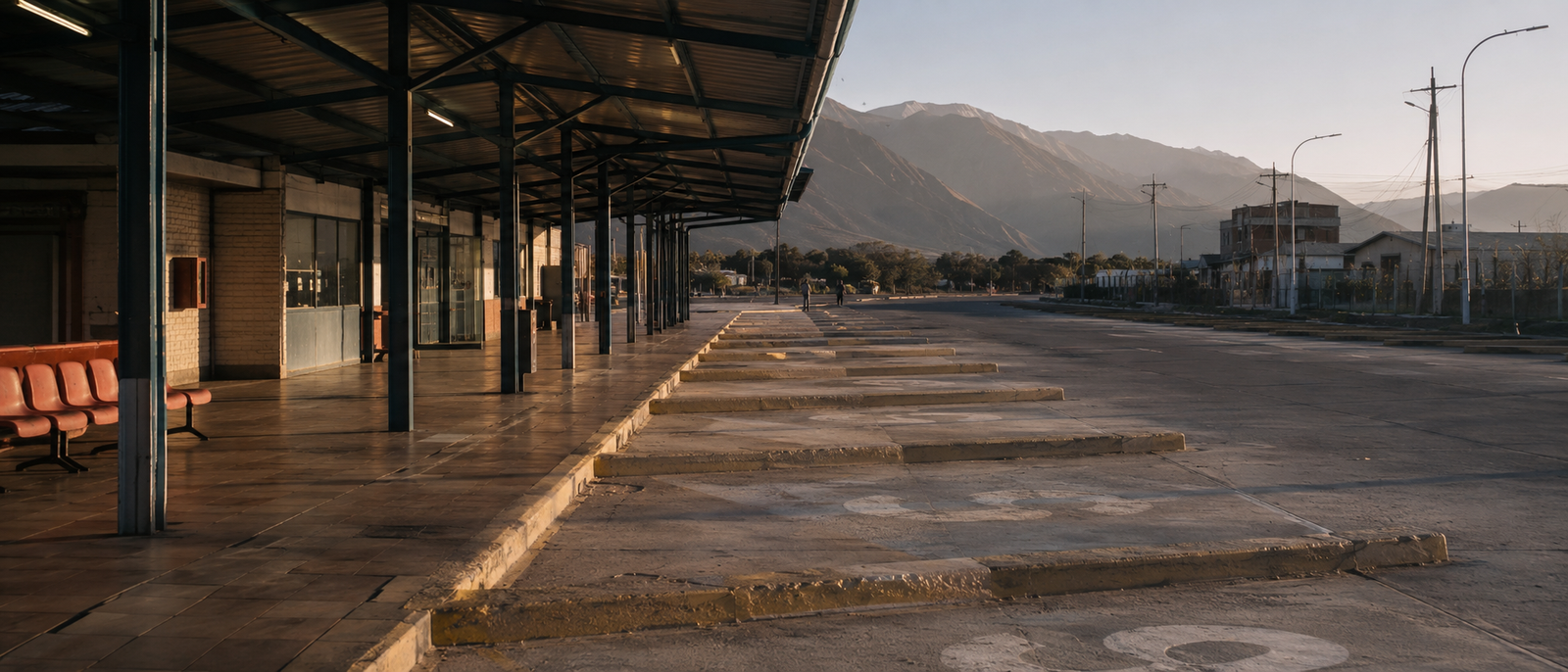 Andenes vacíos de un terminal de buses al amanecer, con cerros al fondo.
